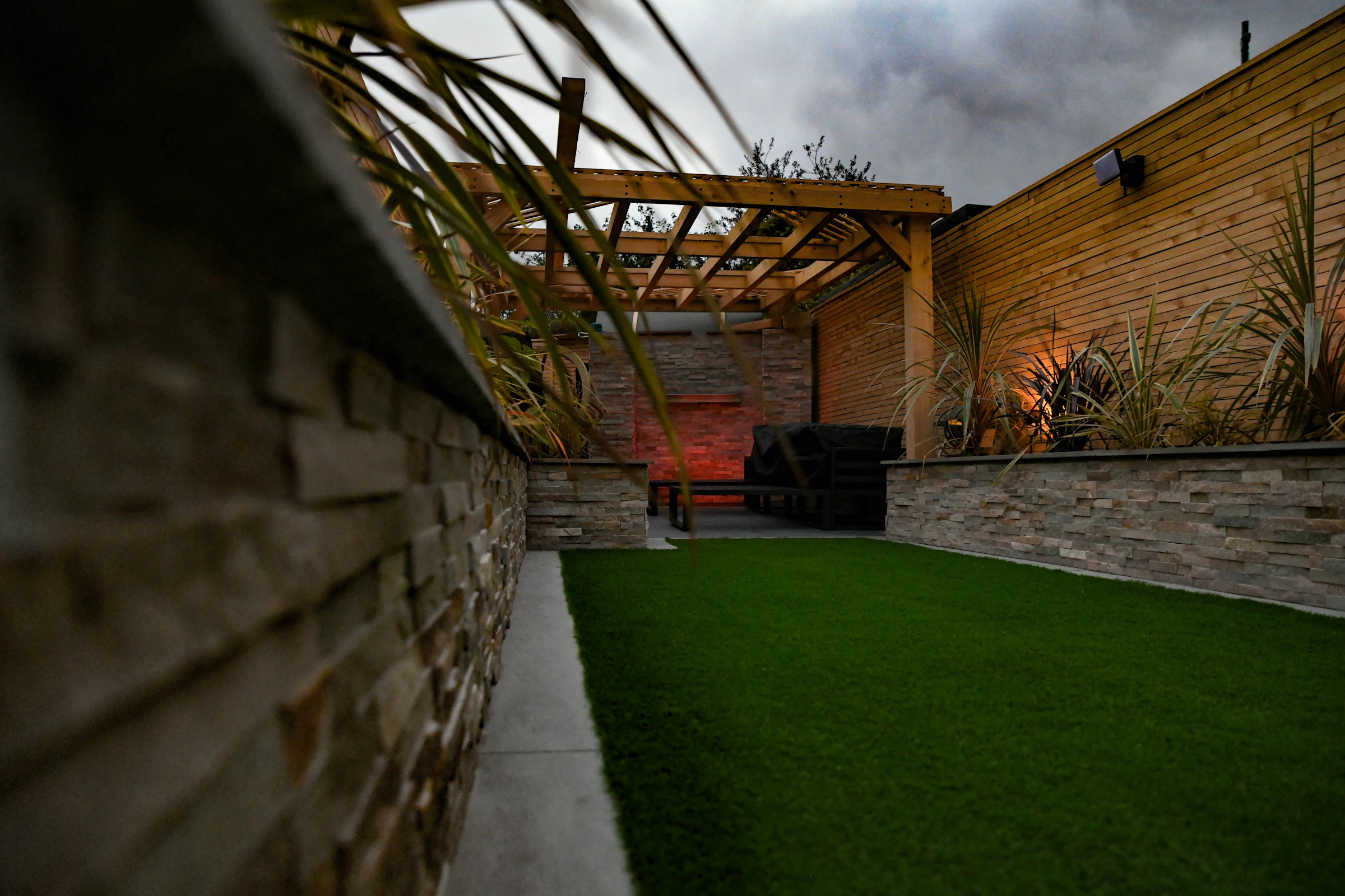 Contemporary courtyard with a pergola, raised planting, and green turf